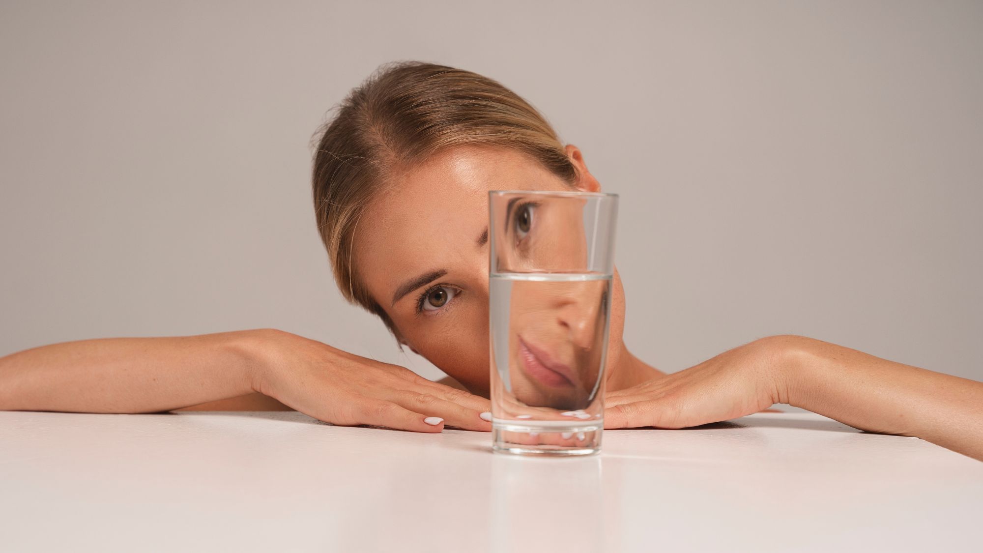 A girl hiding her face behind a glass of water facing rough skin and skin care issues