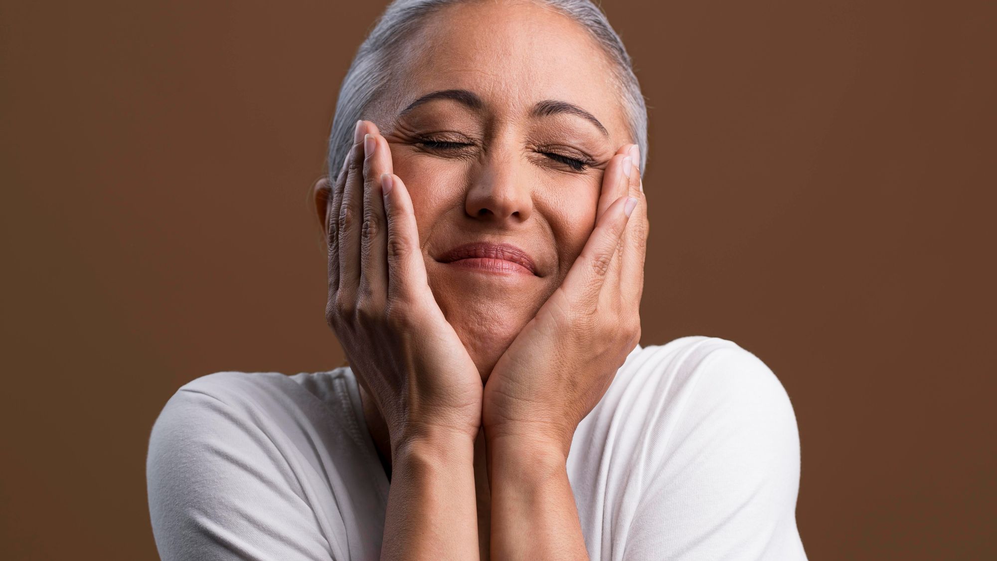 A woman in her menopause span feeling relaxed while gently holding her face skin