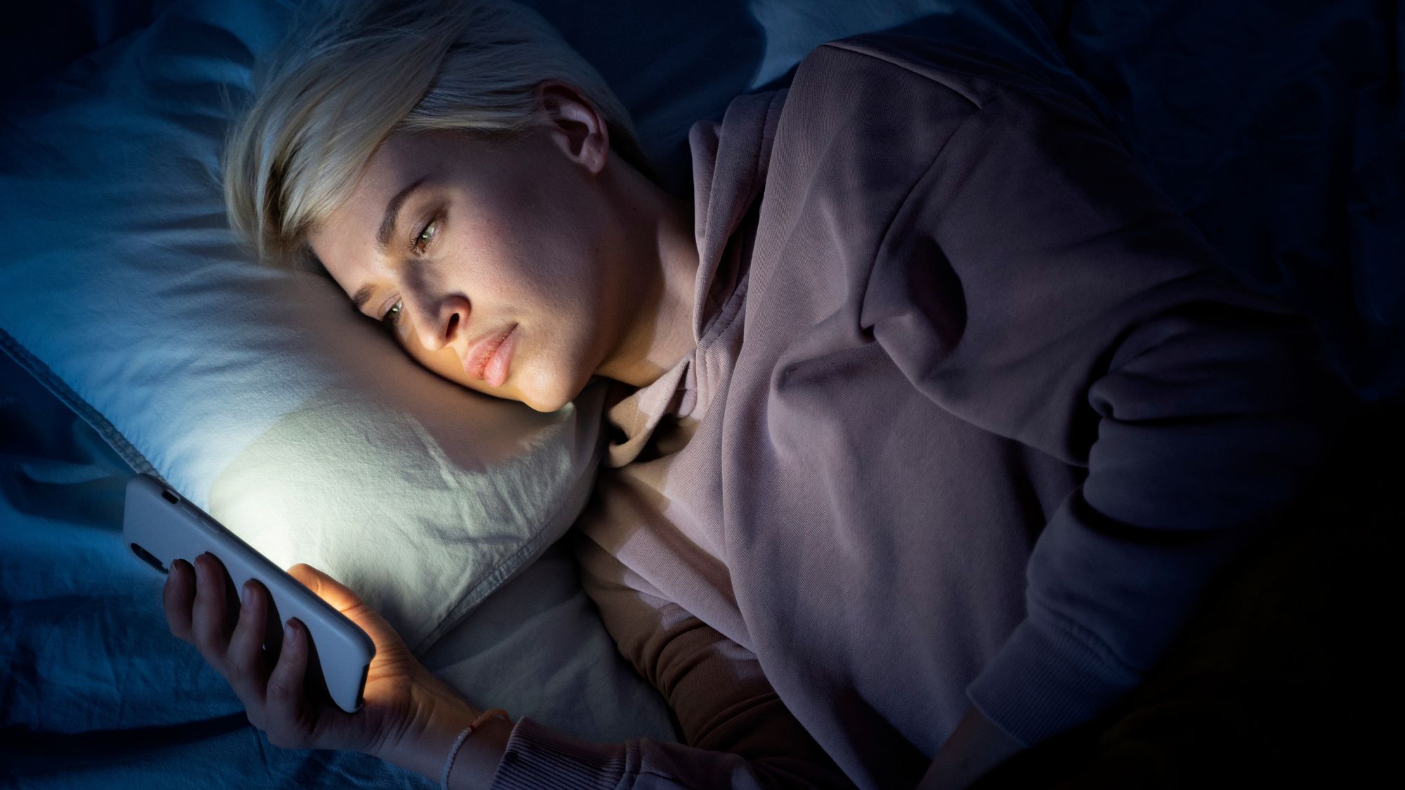 A woman using phone late in her bed, worried and facing rough skin and skin care issues